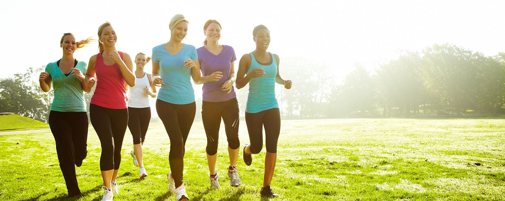 Team of young women jogging together on a large green field